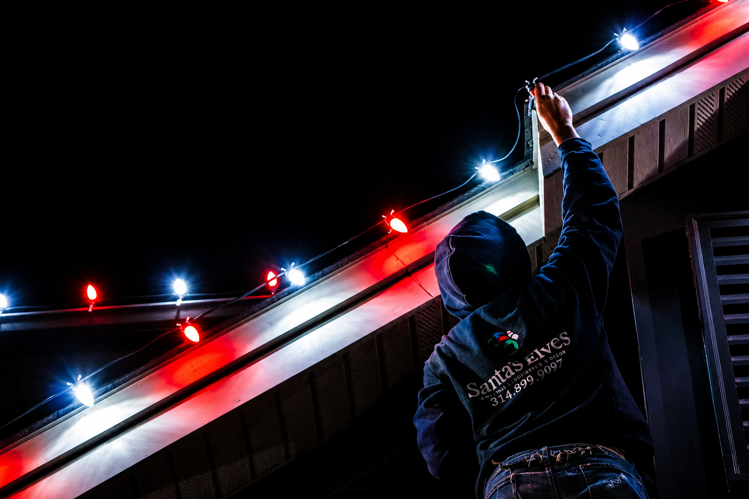 Santa's Elves crew member hanging Christmas lights along a roofline