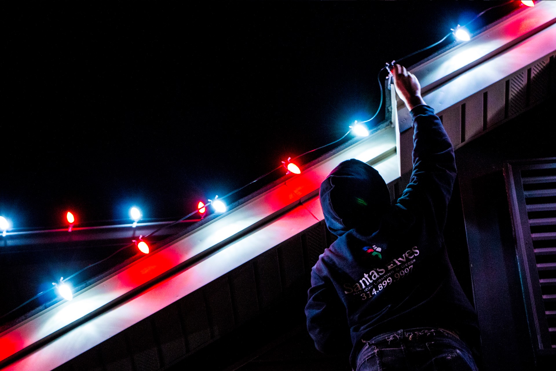 Santa's Elves installer mounting red and white Christmas lights at night